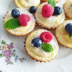 Mini serniczki bez spodu, udekorowane malinami, borówkami i listkami mięty, posypane cukrem pudrem.