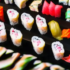 Różnorodne sushi: rolki z różowym nadzieniem i żółtym omletem, kawałki tuńczyka, zielone i pomarańczowe dodatki. Tak wygląda sushi.