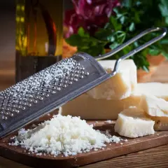 Tarka z grudkami sera, obok kawałki sera Grana Padano i parmezan. W tle butelka oliwy i zielenina.