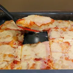 Pyszna, domowa pizza z blachy, z ciągnącym się serem i szynką, właśnie kroimy pierwszy kawałek.