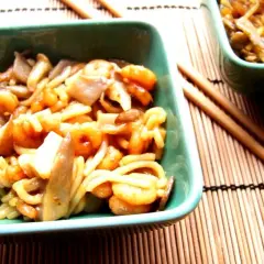 Pyszne krewetki w sosie teriyaki z makaronem i grzybami w zielonej miseczce, gotowe do jedzenia pałeczkami.