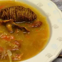 Talerz z żurkiem, w którym widać ziemniaka, grzyby i kiełbasę.