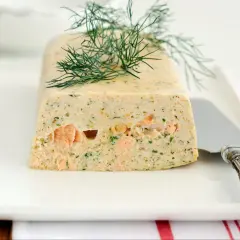 Elegancka terrina z łososia, ozdobiona gałązką koperku, prezentuje się apetycznie na białym talerzu.
