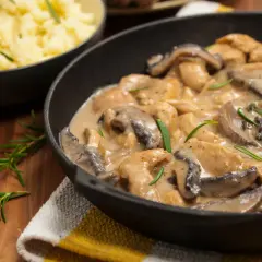 Schab w sosie borowikowym, podany w żeliwnej patelni, z gałązkami rozmarynu. Obok miska z purée ziemniaczanym.
