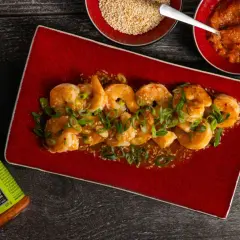 Soczyste krewetki z patelni w sosie z imbirem i chili, posypane szczypiorkiem i sezamem. Obok miseczki z sezamem i pastą chili.