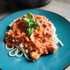 Pyszny makaron z mięsem mielonym w kremowym sosie śmietanowo serowym, udekorowany listkiem bazylii.