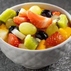Kolorowa sałatka z owocami: truskawki, kiwi, winogrona, mango i borówki w białej miseczce.