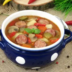 Gęsta zupa węgierska z kiełbasą, ziemniakami, papryką i pieczarkami, udekorowana listkiem bazylii.