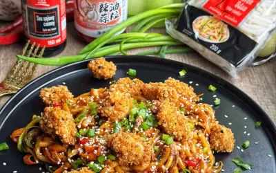 Pyszny makaron udon z kurczakiem w panierce, polany sosem sojowym, posypany sezamem i szczypiorkiem.