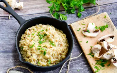 Kremowe risotto z warzywami, posypane natką pietruszki, obok świeże pieczarki na desce.
