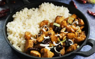 Pyszny kurczak kung pao z ryżem, orzeszkami ziemnymi i szczypiorkiem w żeliwnej patelni.
