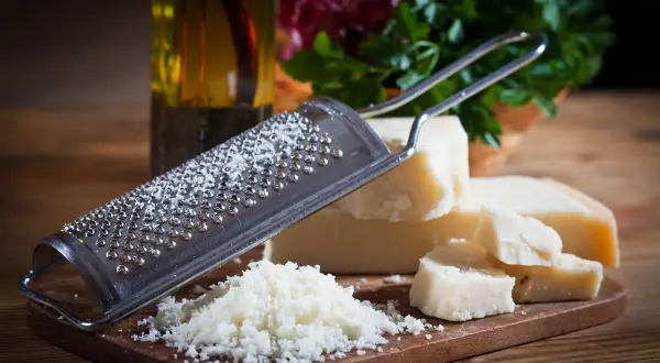Tarka z grudkami sera, obok kawałki sera Grana Padano i parmezan. W tle butelka oliwy i zielenina.