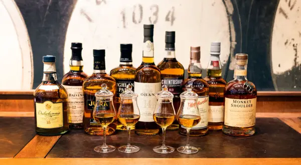 Rząd butelek whisky, w tym Dalwhinnie, Balvenie, Jura, Oban, Glenmorangie, Monkey Shoulder. Idealne na tanie dobre whisky.