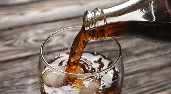 Nalewanie ciemnego napoju z butelki do szklanki z lodem. Zastanawiasz się, ile kalorii ma whisky z colą zero?
