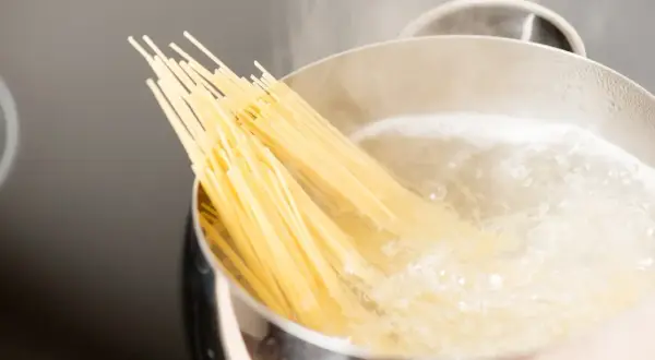 Kluska spaghetti zanurza się w gotującej wodzie. Czy wode na makaron sie soli? Tak, aby nadać jej smak.
