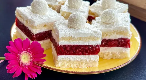 Pyszne ciasto rafaello z malinami, udekorowane wiórkami kokosowymi i malinową galaretką. Obok różowa gerbera.