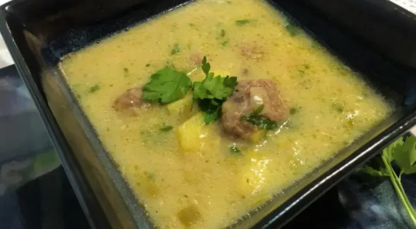Aksamitna zupa porowo serowa z pulpecikami, ozdobiona natką pietruszki, w kwadratowej misce.