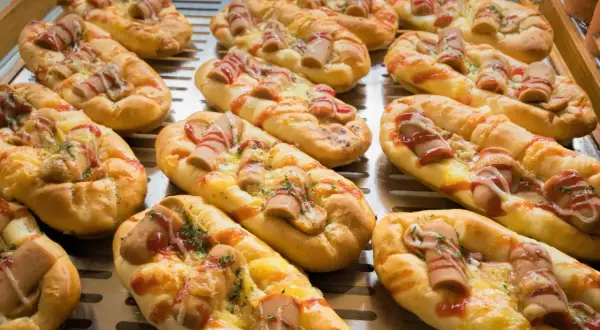 Pyszne zapiekanki z parówkami, posypane serem i keczupem, kuszą swoim wyglądem na tacy.