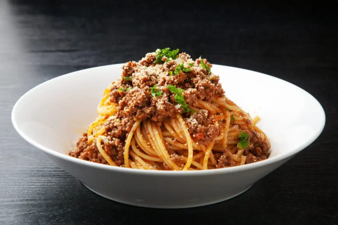 Spaghetti z sosem bolońskim i parmezanem w białej misce.