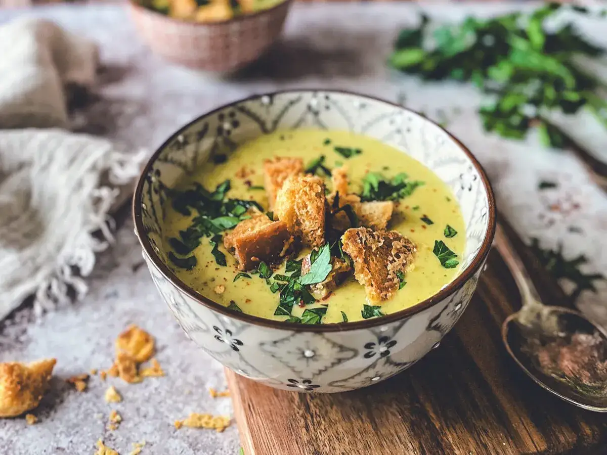 Aksamitna zupa brokułowa z serem cheddar, udekorowana chrupiącymi grzankami i świeżą natką pietruszki.