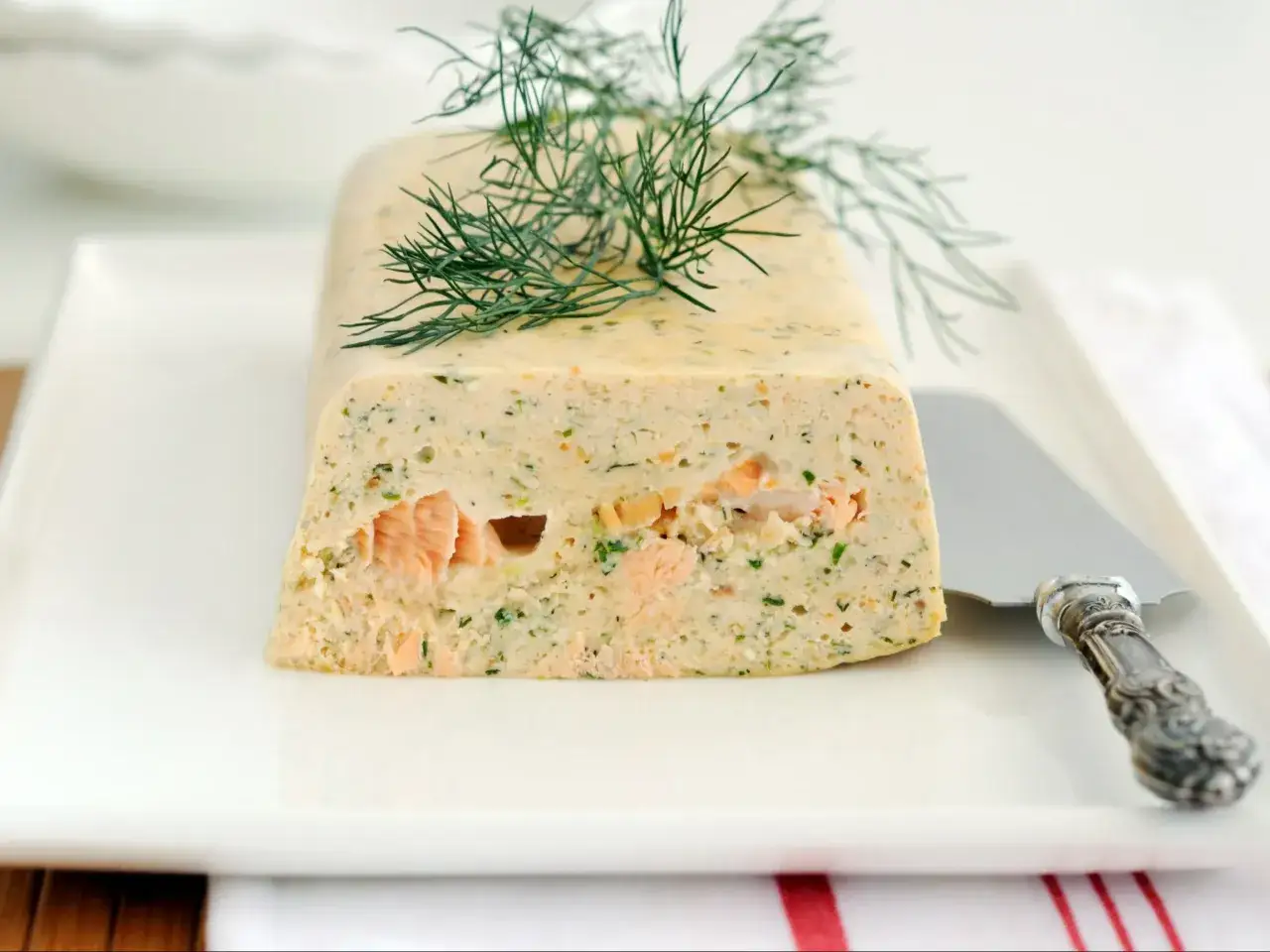 Elegancka terrina z łososia, udekorowana gałązką koperku, prezentuje się apetycznie na białym talerzu.