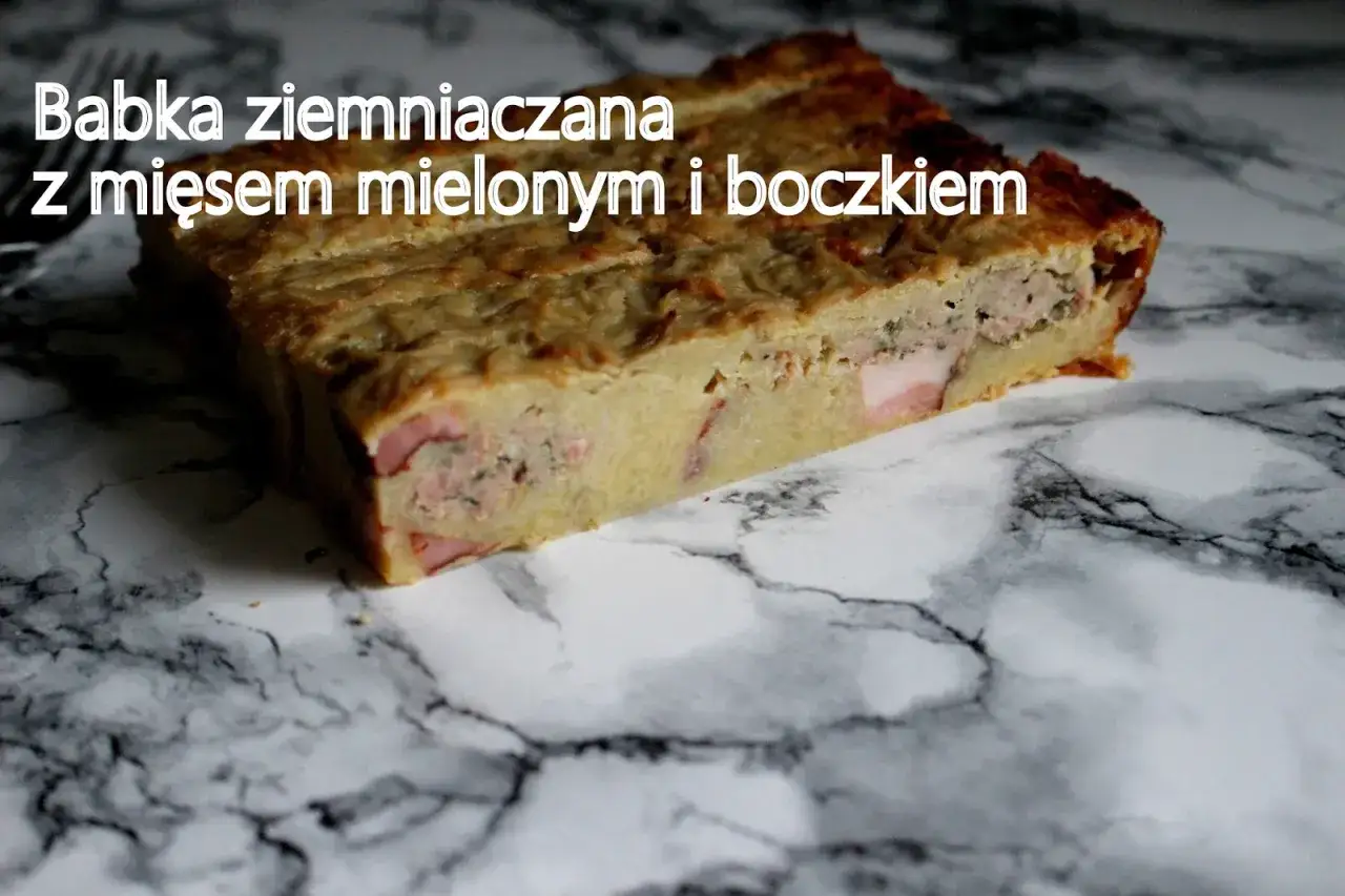 Kawałek babki ziemniaczanej z mięsem mielonym i kawałkami boczku, prezentuje się apetycznie na marmurowym tle.