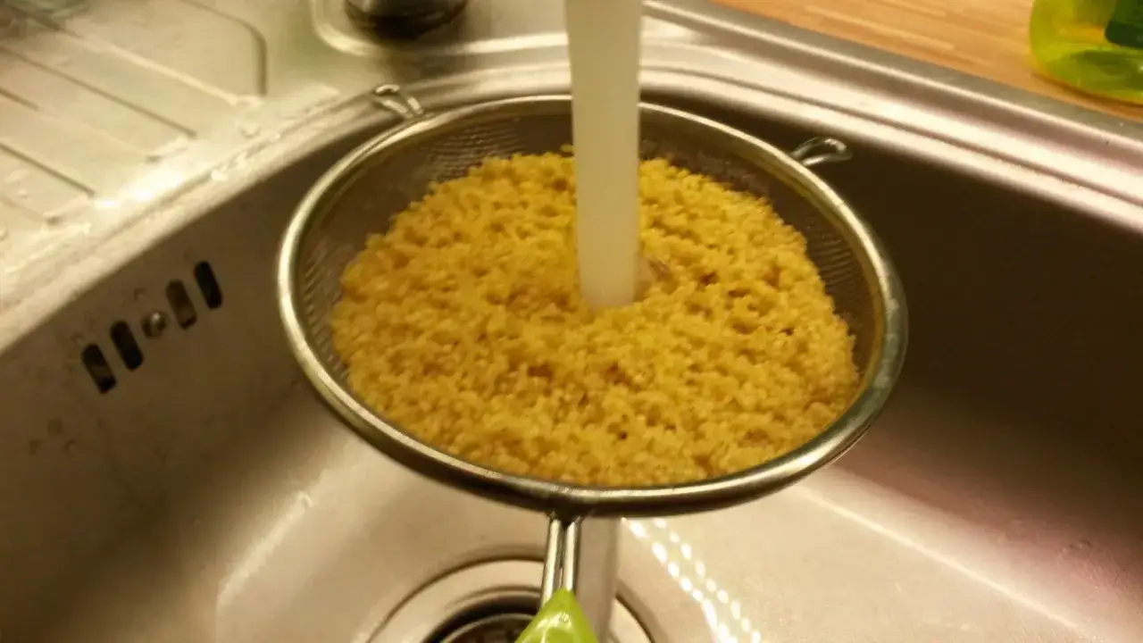 Płukanie kaszy jaglanej na sypko w durszlaku pod bieżącą wodą. Kluczowy krok, by uniknąć grudek.