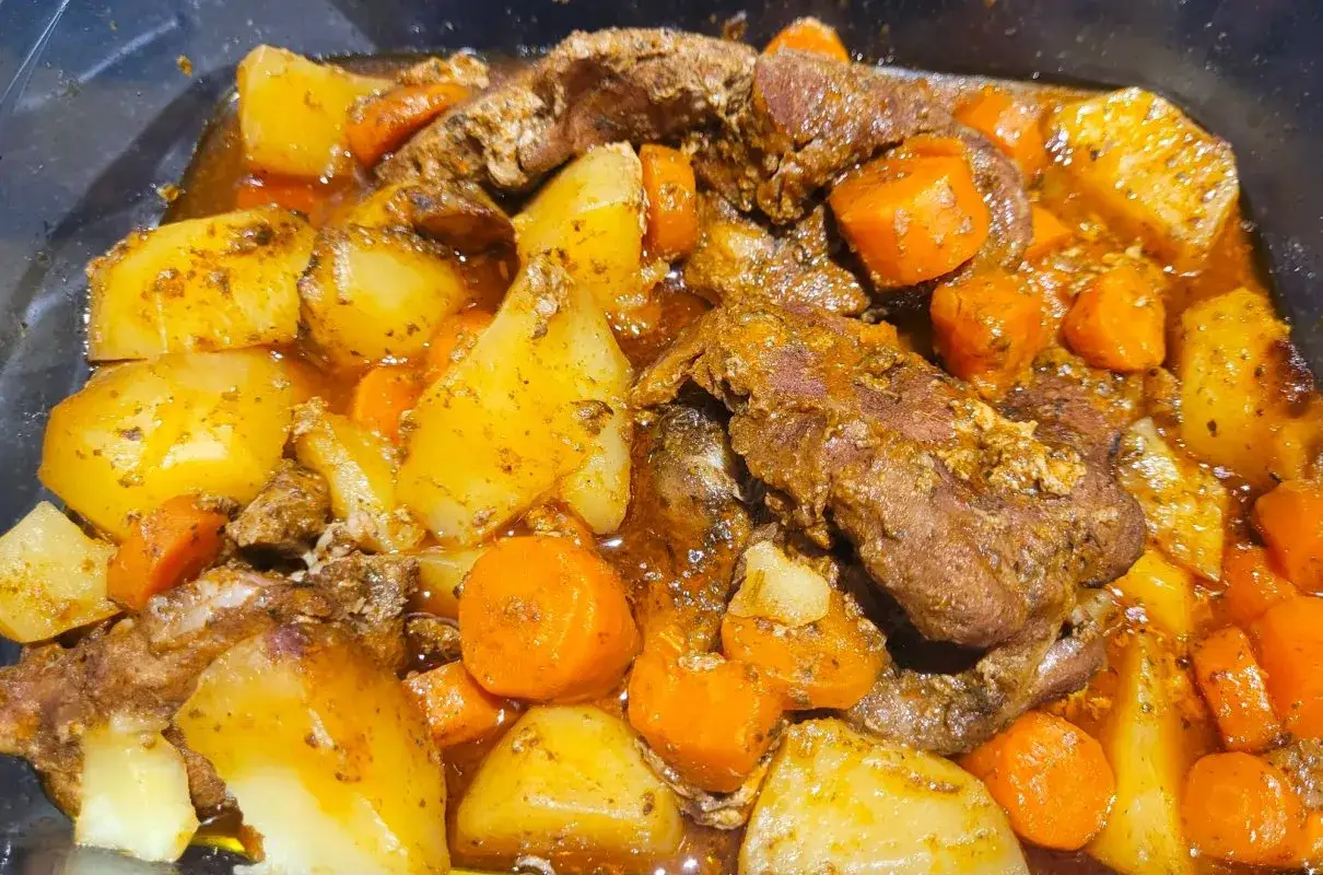 Duszona karkówka z pieczarkami i warzywami, podana w sosie z ziemniakami i marchewką.