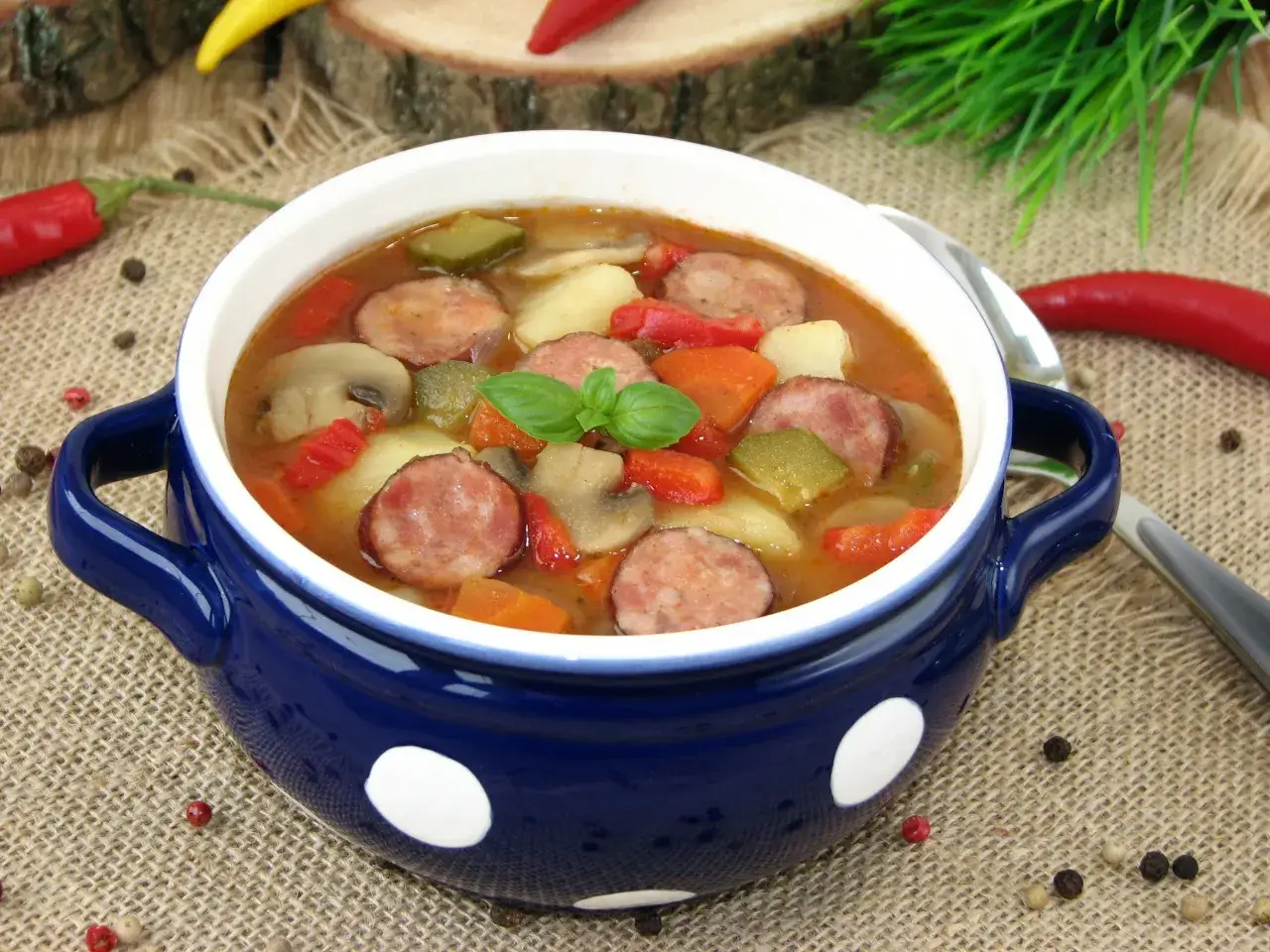 Gęsta zupa węgierska z kiełbasą, ziemniakami, papryką i grzybami, udekorowana bazylią.