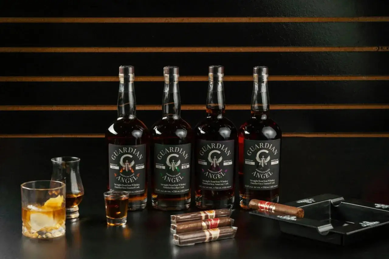 Cztery butelki bourbonu Guardian Angel, kieliszek z lodem, kieliszek degustacyjny i cygara. Poznaj, jak smakuje bourbon.