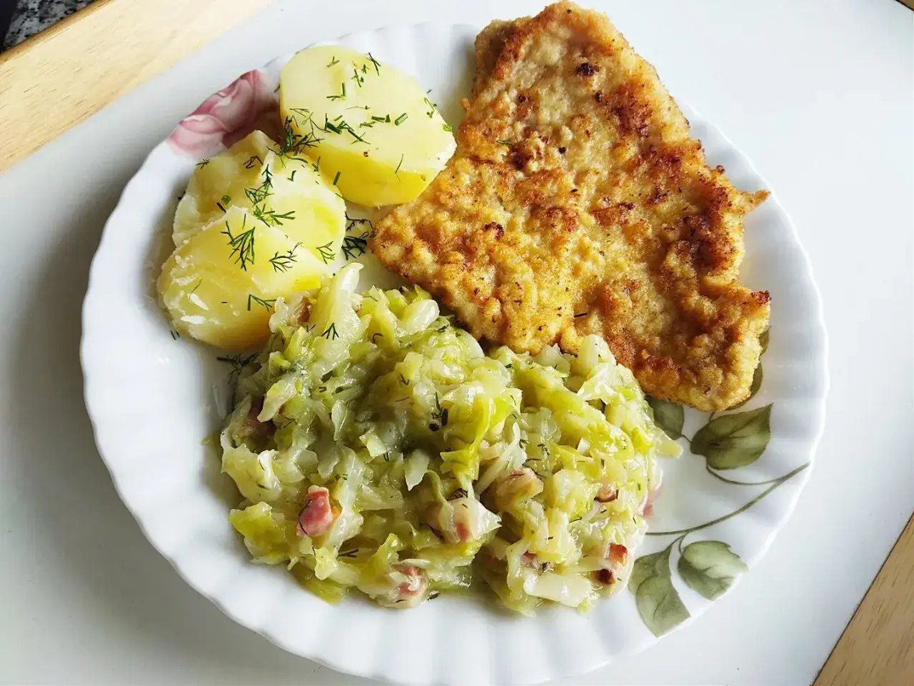 Kapusta zasmażana kiszona z boczkiem, ziemniaki i panierowany kotlet na talerzu. Pyszny, domowy obiad.