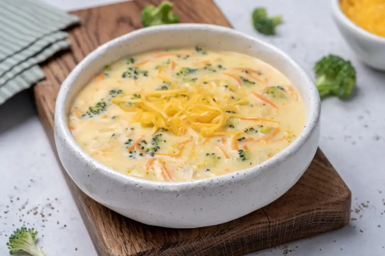 Aksamitna zupa brokułowa z serem cheddar, pełna kawałków brokułów i marchewki, ozdobiona wiórkami żółtego sera.