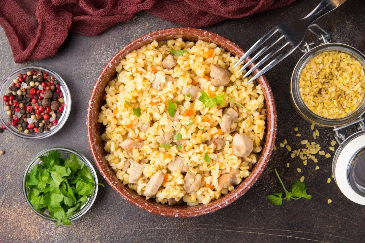 Czy kasza bulgur pasuje do gulaszu? Miska pełna bulguru z kawałkami mięsa i marchewki, obok przyprawy i zielenina.