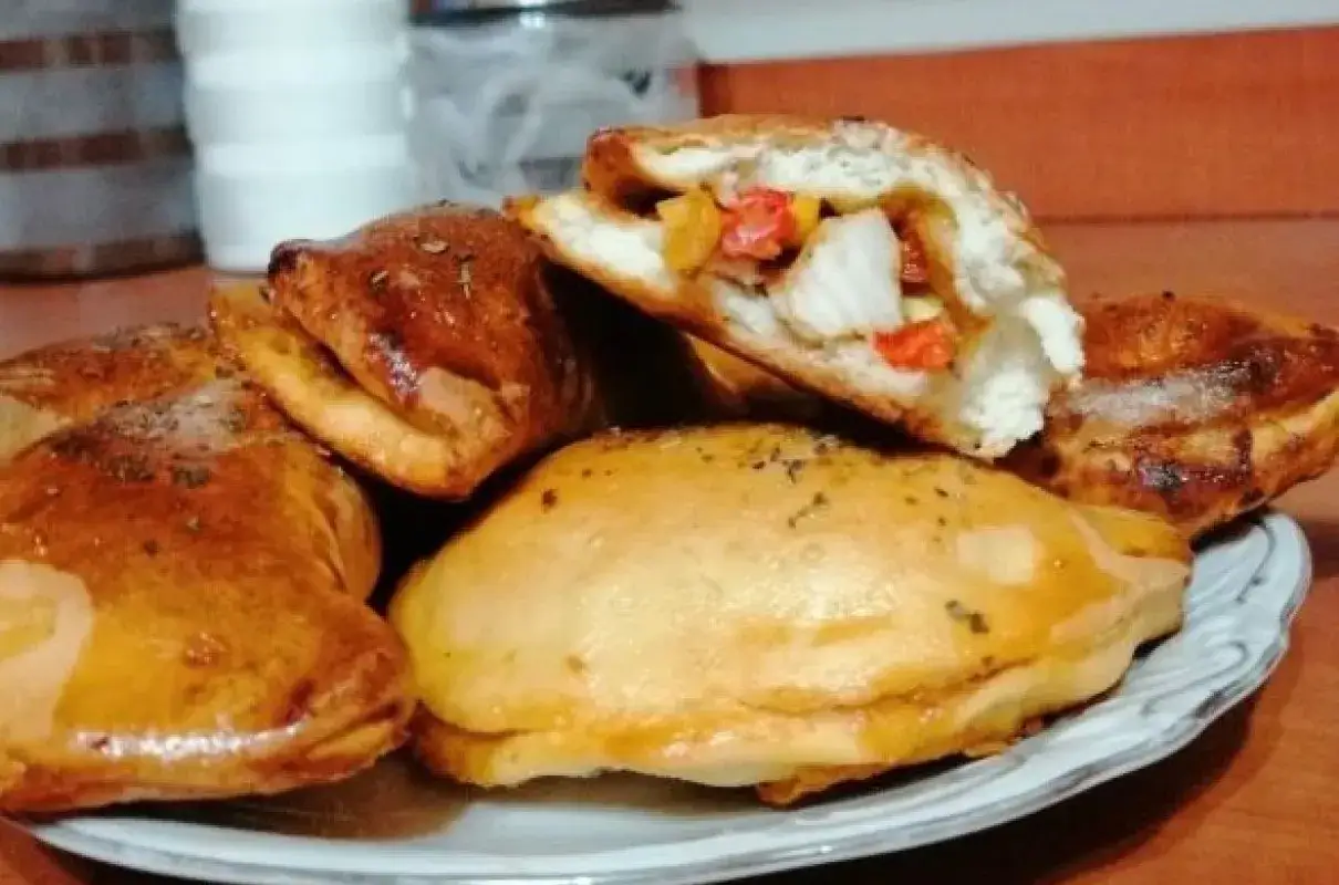 Złociste, pieczone pierogi z kurczakiem gyros i warzywami, jeden przekrojony, ukazujący soczyste nadzienie.